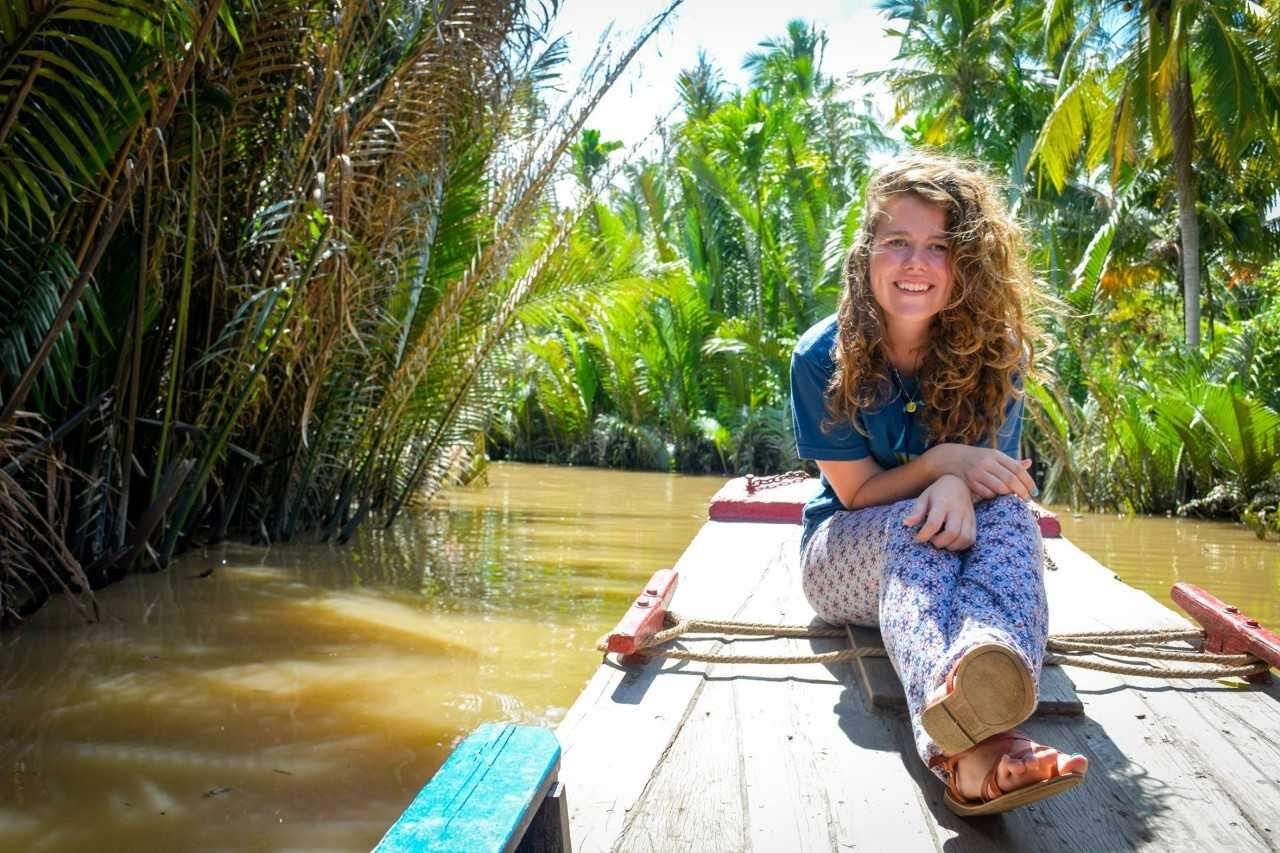 A student on a small river boat surrounded by jungle.